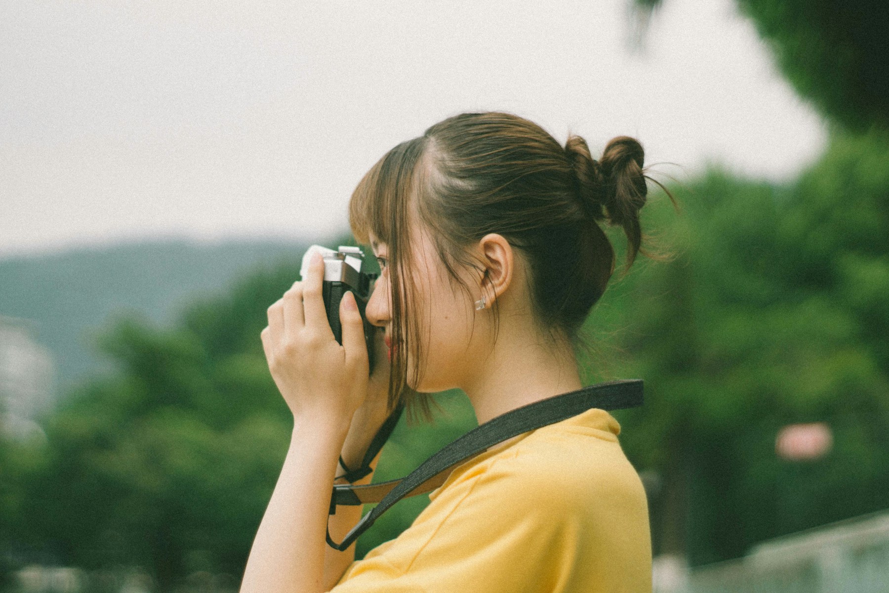 Young woman looking through a film camera outdoors